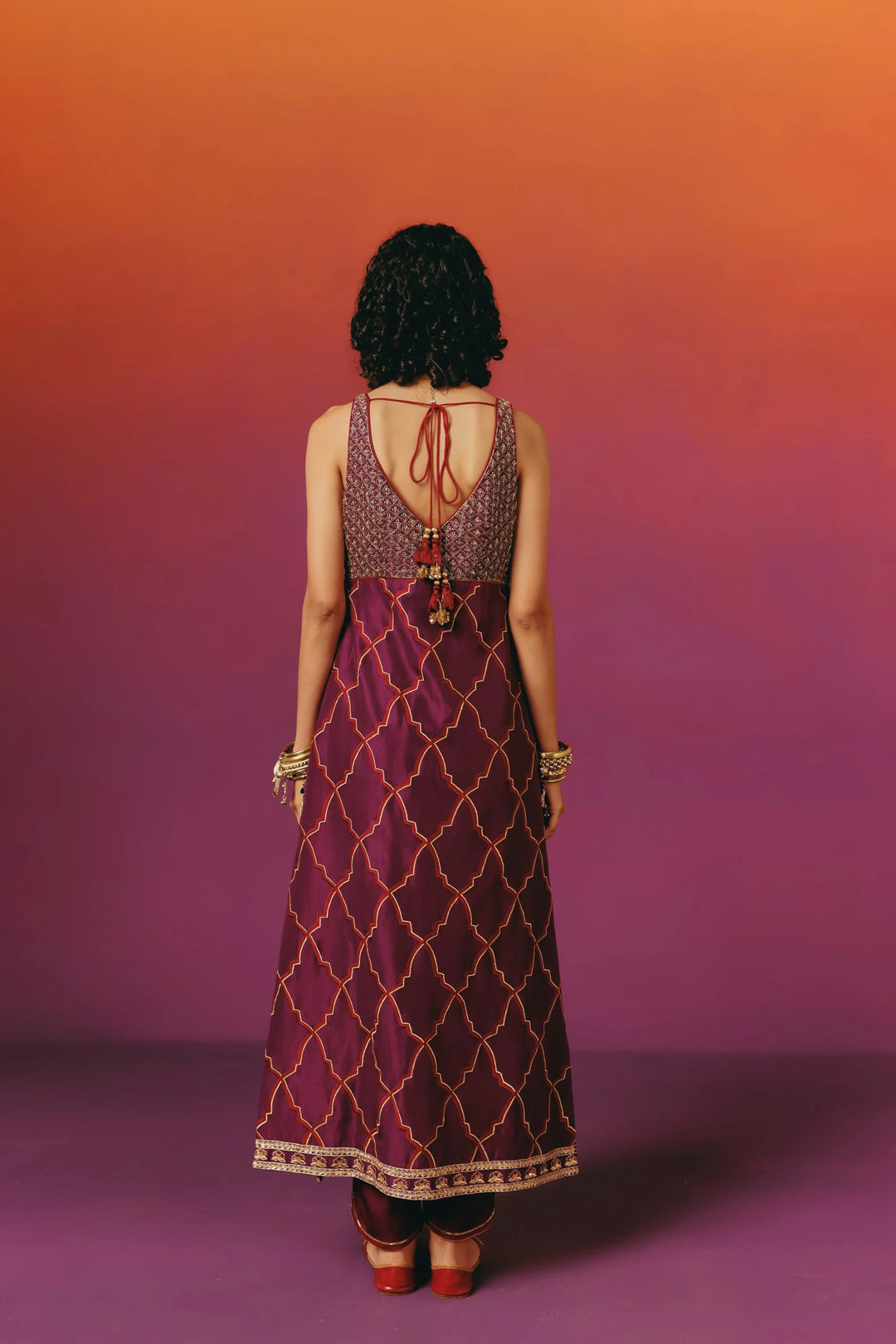 Back view of a model in Warra's sleeveless wine-purple kurta set showing the tie-back straps and gold trellis-embroidered skirt