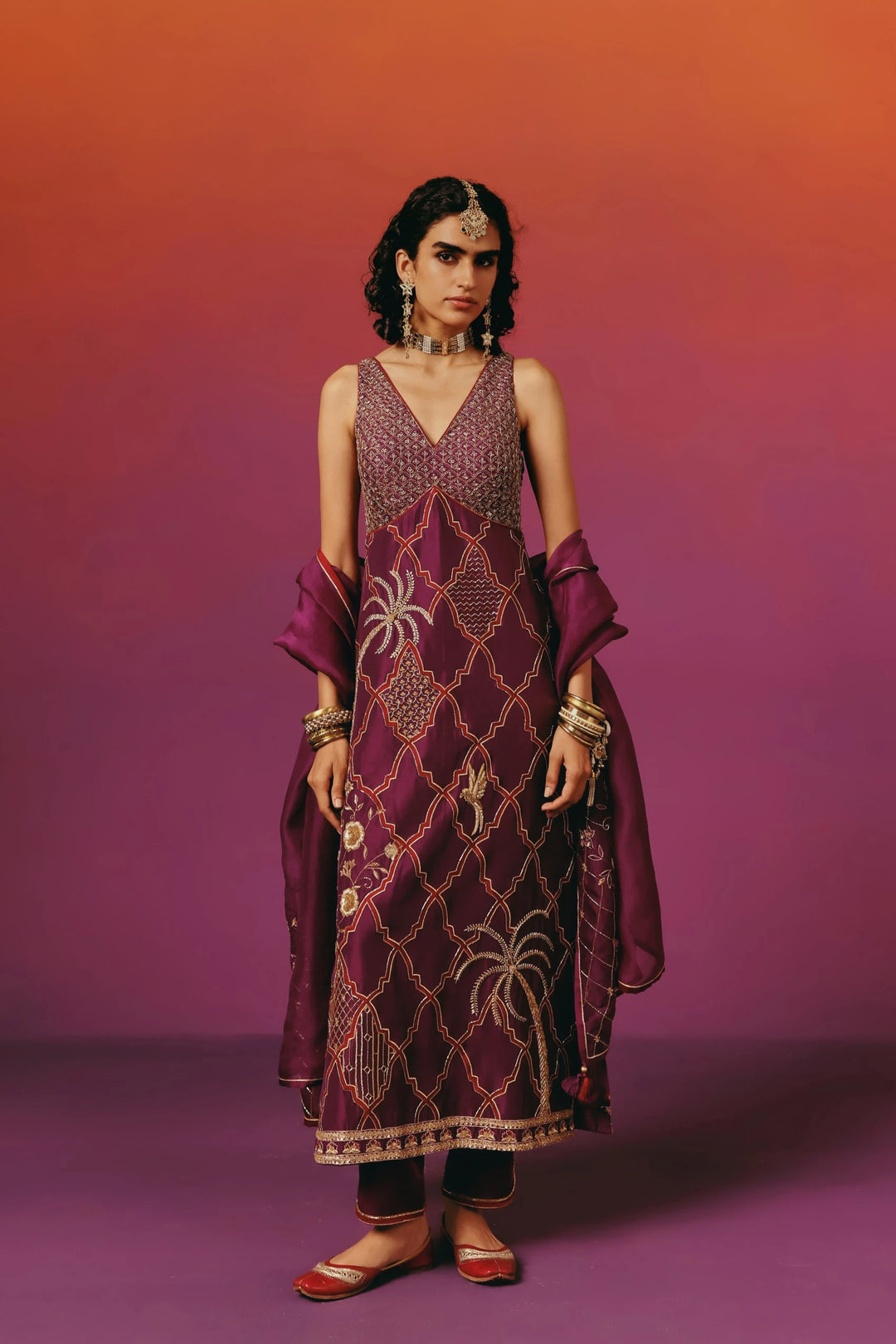 Full-length front view of a model in Warra's sleeveless wine-purple kurta set with a beaded bodice, gold quatrefoil trellis embroidery, palm tree and bird motifs, paired with a matching dupatta
