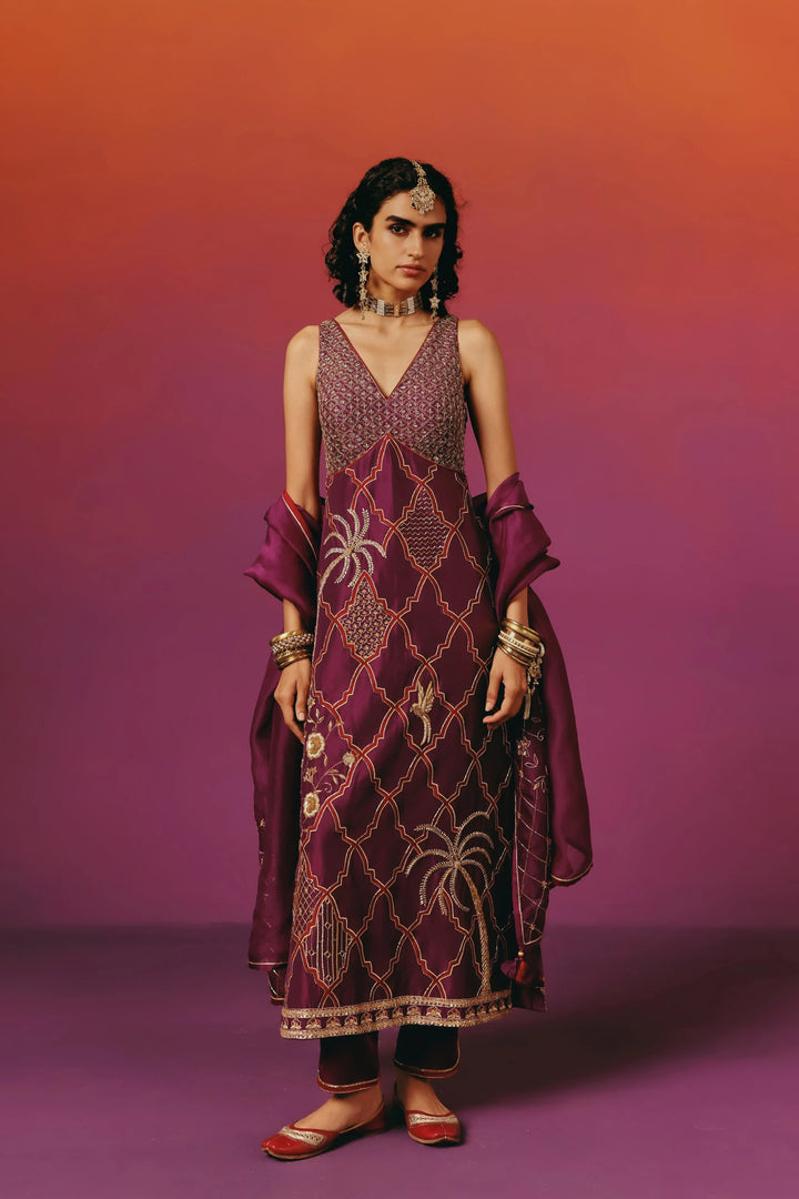 Full-length front view of a model in Warra's sleeveless wine-purple kurta set with a beaded bodice, gold quatrefoil trellis embroidery, palm tree and bird motifs, paired with a matching dupatta