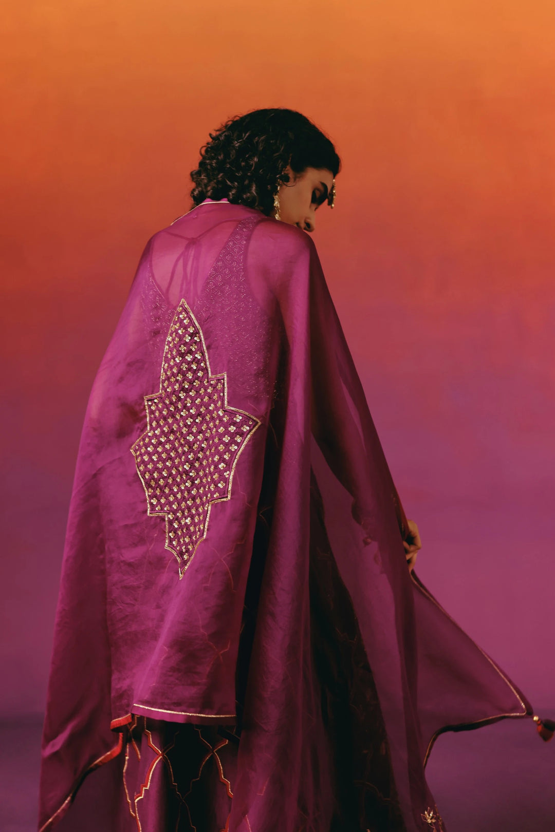 Back view of a model in Warra's wine-purple kurta set with the matching dupatta draped cape-like over the shoulders, showing a gold sequin star motif