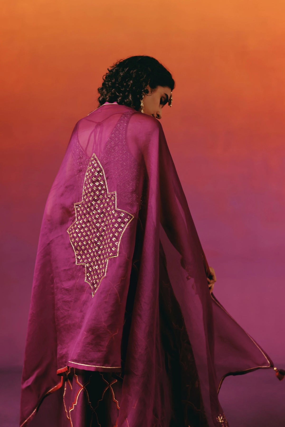 Back view of a model in Warra's wine-purple kurta set with the matching dupatta draped cape-like over the shoulders, showing a gold sequin star motif