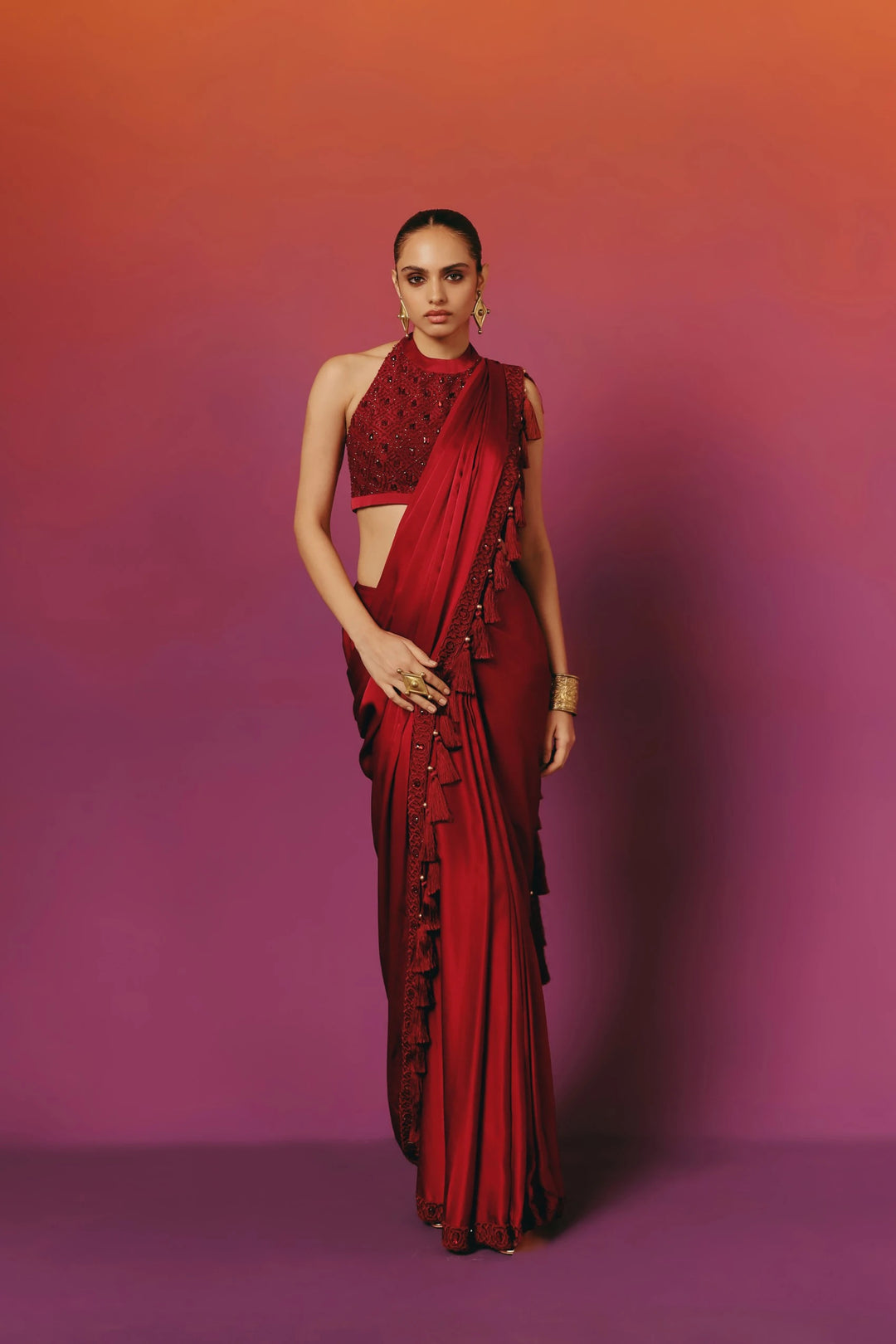 Full-length front view of a model in Warra's crimson pre-draped silk saree with a beaded halter-neck blouse and a beaded tassel trim running down the pallu