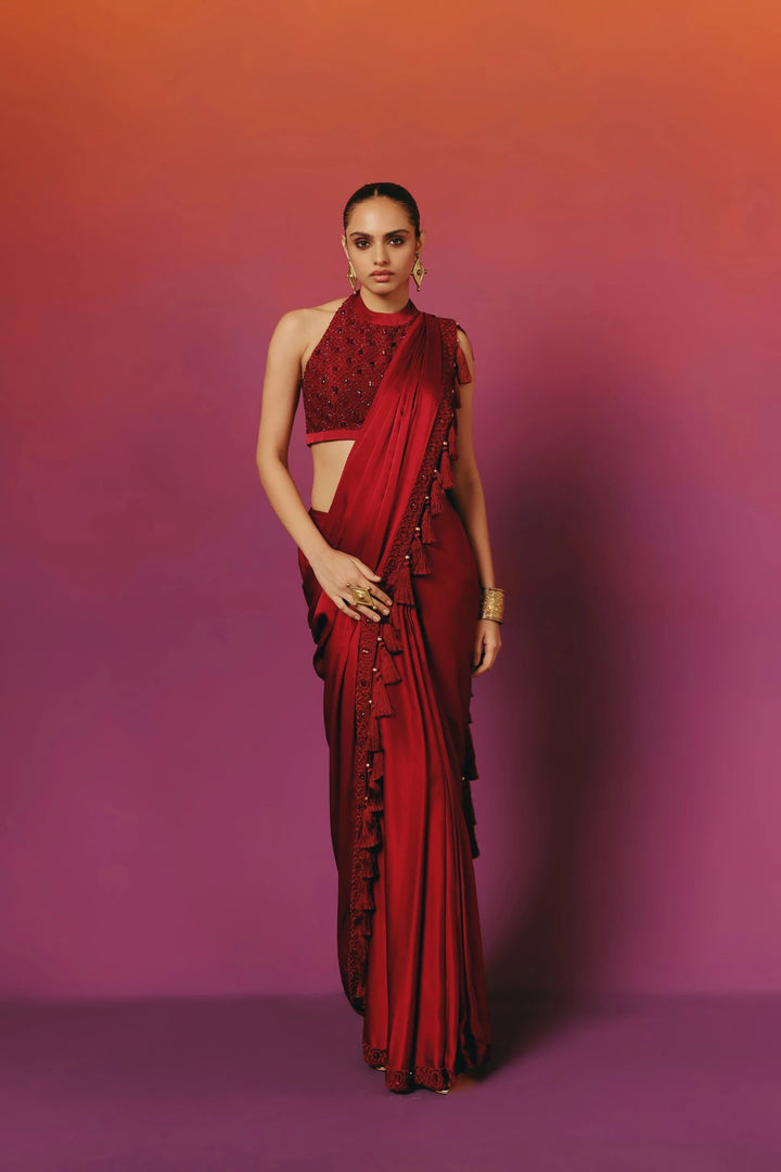 Full-length front view of a model in Warra's crimson pre-draped silk saree with a beaded halter-neck blouse and a beaded tassel trim running down the pallu