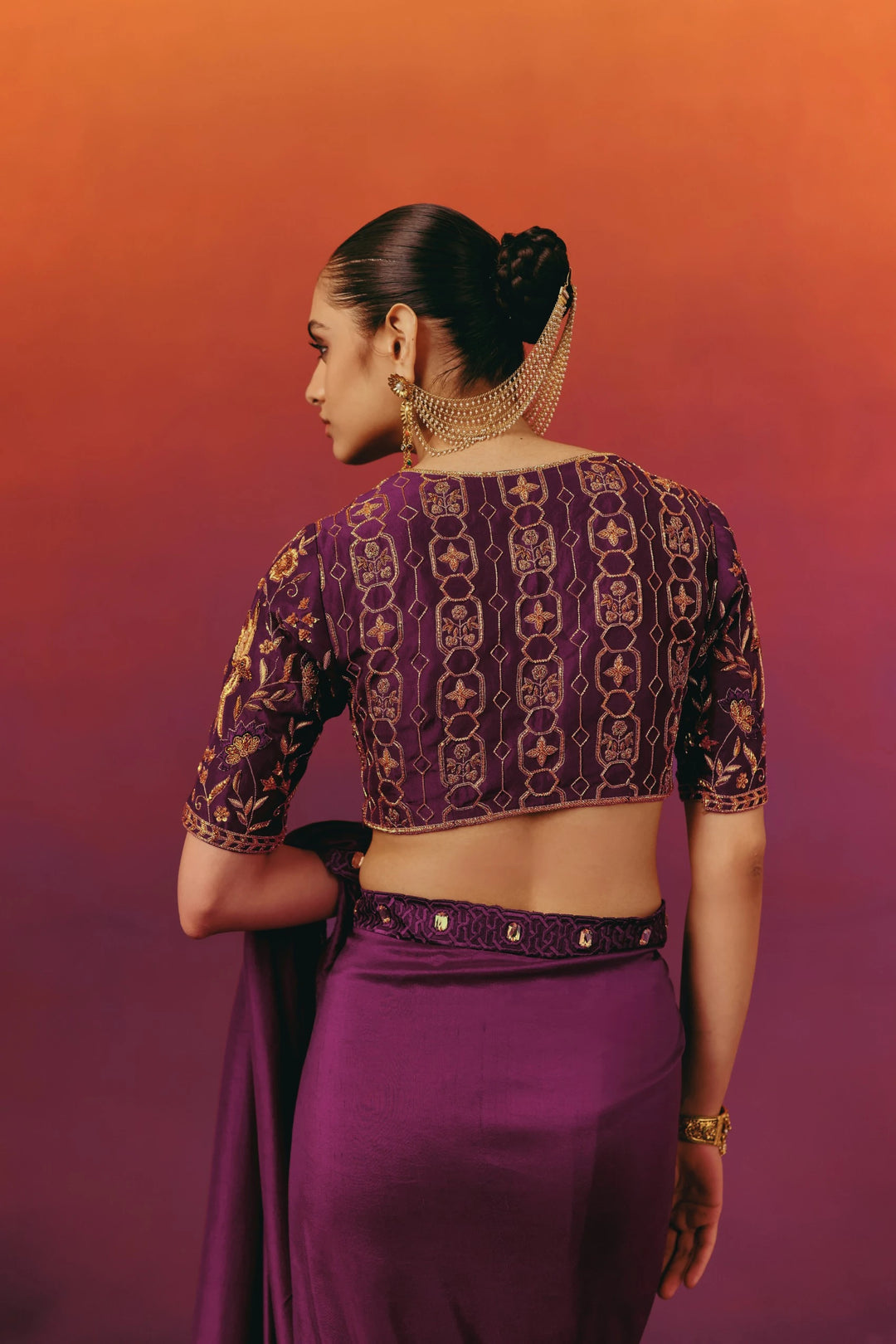 Back view of the hand-embroidered blouse on Warra's purple silk saree, showing a geometric trellis pattern in gold and rust thread work