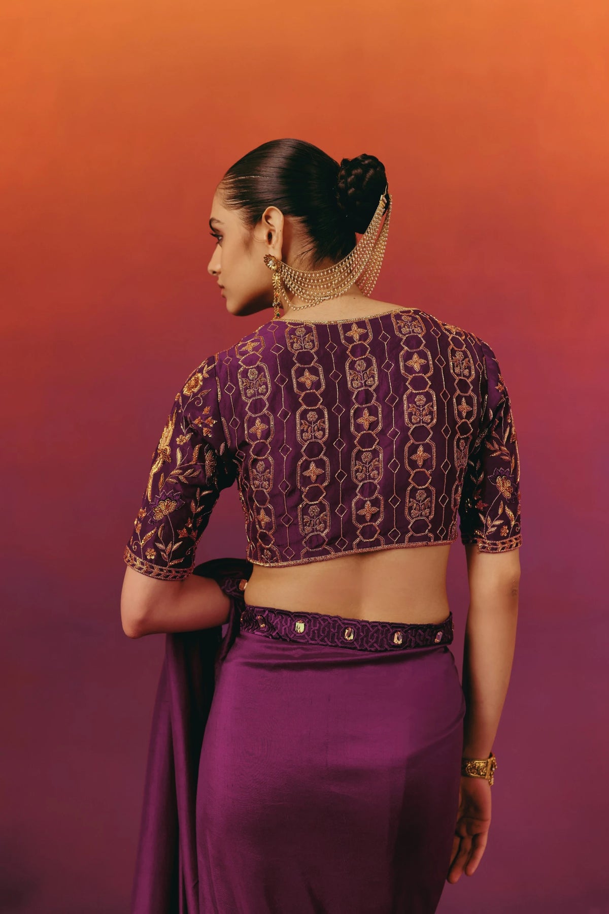 Back view of the hand-embroidered blouse on Warra's purple silk saree, showing a geometric trellis pattern in gold and rust thread work