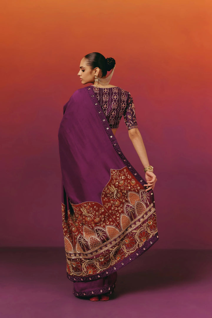 Back view of a model in Warra's purple silk saree with the pallu draped over the shoulder, showing the rust-red hand-embroidered palm tree border in movement