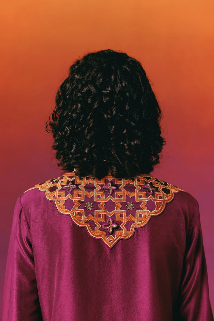 Close-up back view of a model in Warra's magenta silk kaftan showing the star-and-diamond embroidered yoke pattern in orange and gold