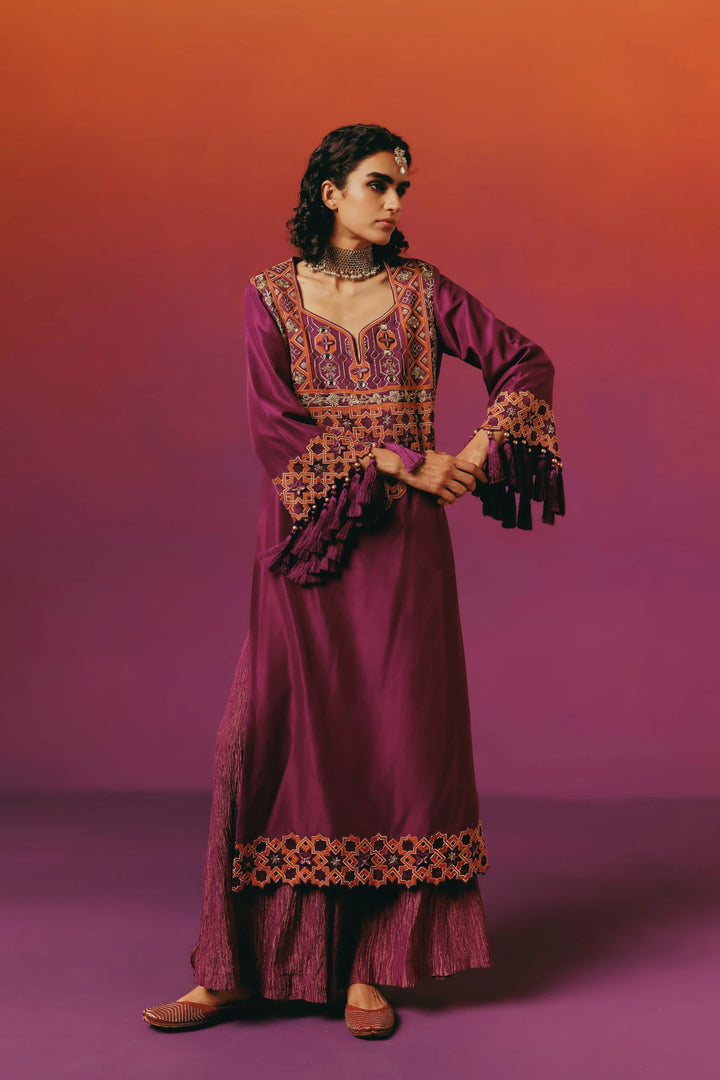 Full-length side view of a model in Warra's magenta silk kaftan with orange-bordered star embroidery, tasselled sleeve cuffs and matching shimmer palazzo pants