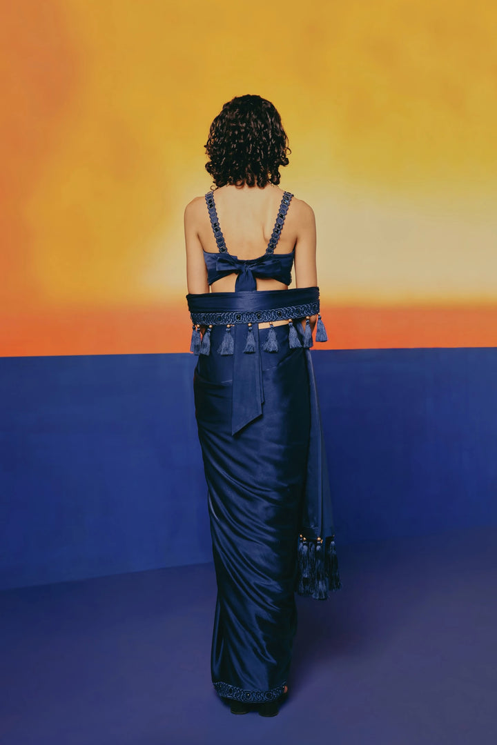 Back view of a model in Warra's Crystal Blue Tassel Saree showing the bow-tied blouse back and tasseled waist sash over a sheath skirt