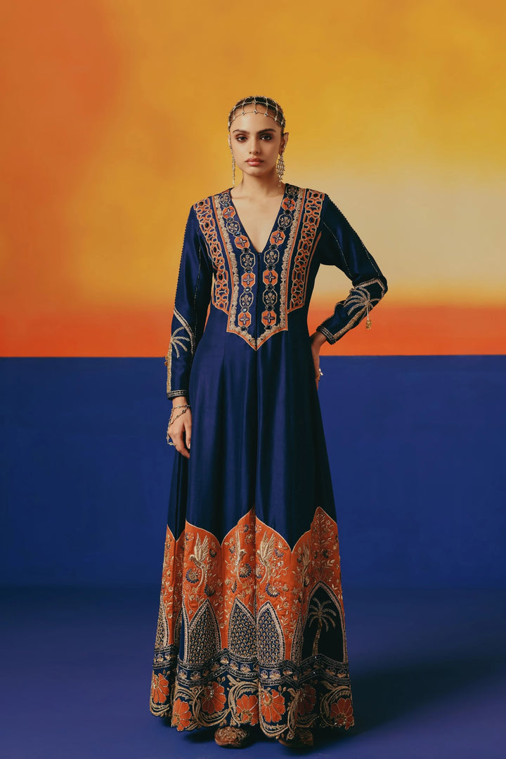 Front view of a model in Warra's navy silk anarkali with an orange-and-gold embroidered yoke and hem border, standing with one hand on the hip