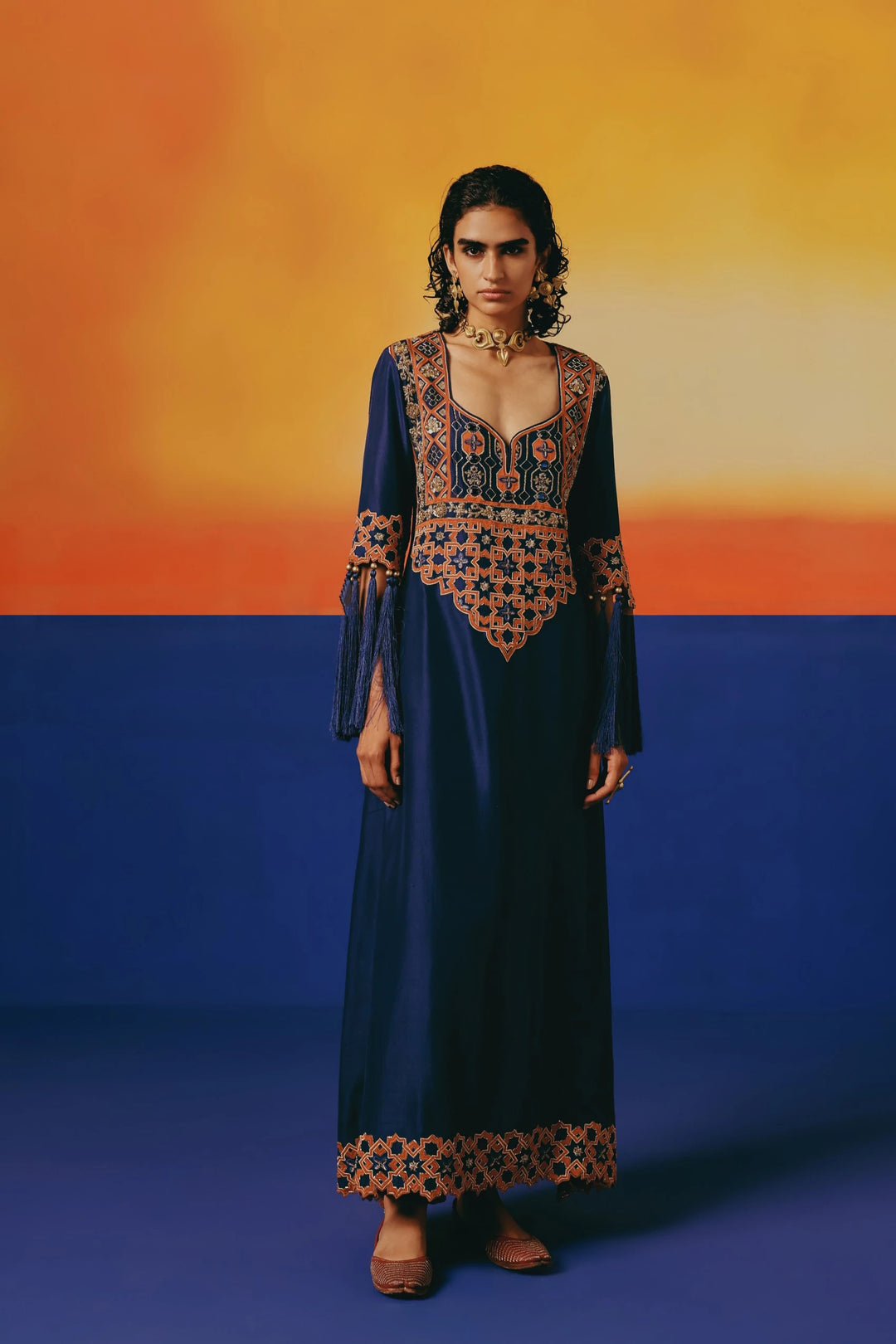 Full-length front view of Warra's navy silk kaftan with orange geometric embroidery on the neckline and an embellished hem