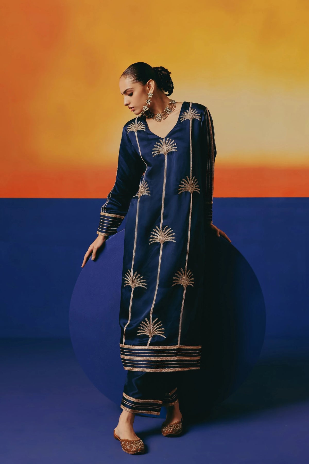 A navy blue long kurta by Warra with gold palm tree embroidery and striped cuffs and hem, paired with matching pants.