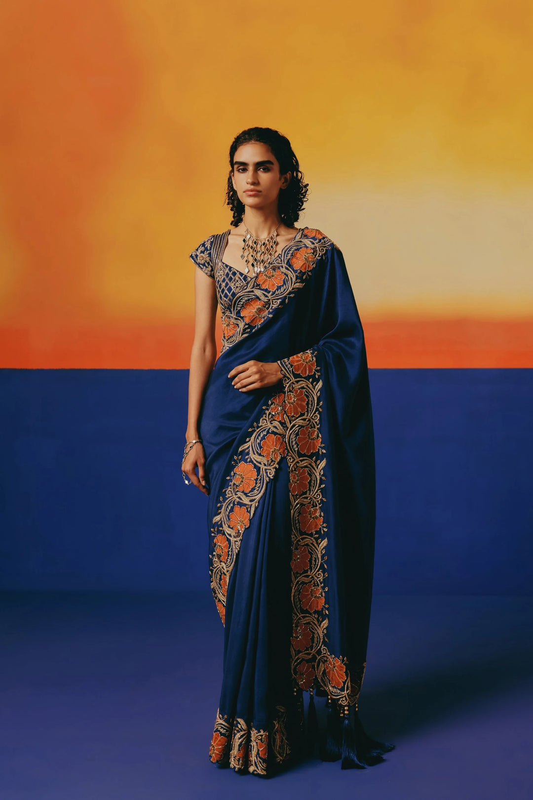 Full-length front view of a model in Warra's navy silk saree with an orange floral embroidered border along the pallu