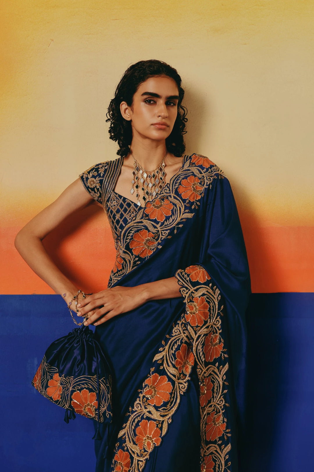 Three-quarter view of a model in Warra's navy silk saree carrying a matching embroidered potli bag with orange floral detailing