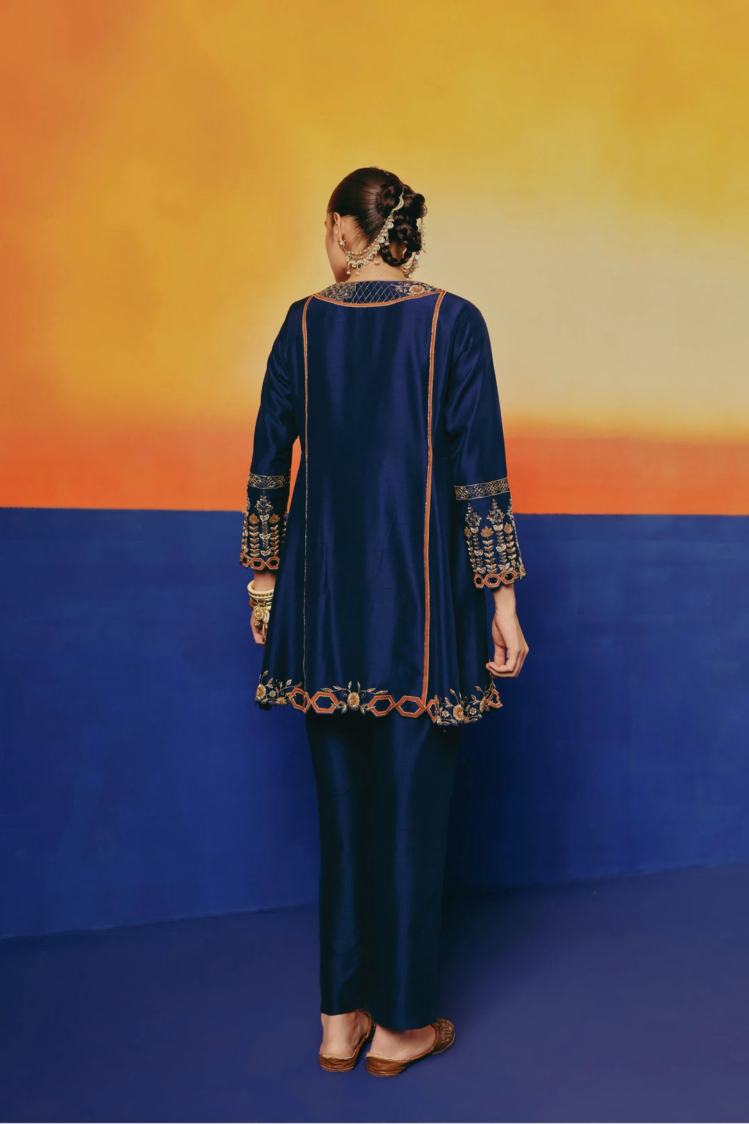 Back view of a model in Warra's navy silk tunic showing the gold embroidered yoke and flared hemline over matching pants