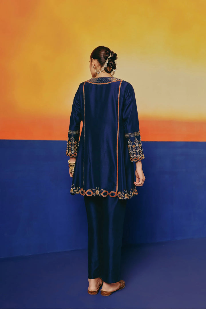 Back view of a model in Warra's navy silk tunic showing the gold embroidered yoke and flared hemline over matching pants