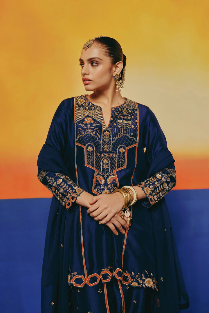 Close-up front view of a model in Warra's navy silk tunic showing dense gold embroidery on the yoke and jewelled headpiece