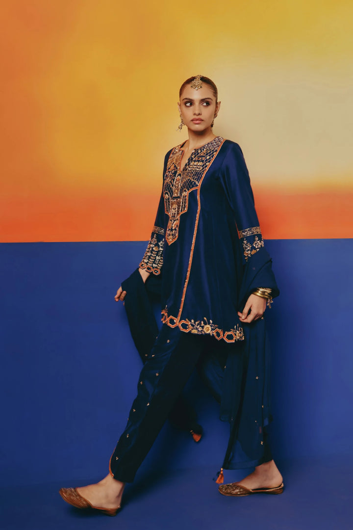 Three-quarter walking view of a model in Warra's navy silk tunic with gold embroidered yoke and draped dhoti-style pants