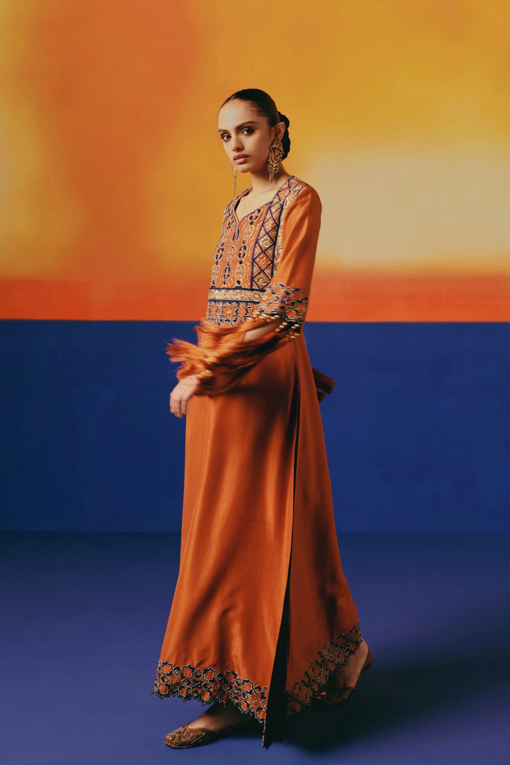 Close-up of a model with arms crossed wearing Warra's orange silk kaftan, showing gold bracelet and long tasselled cuff fringe