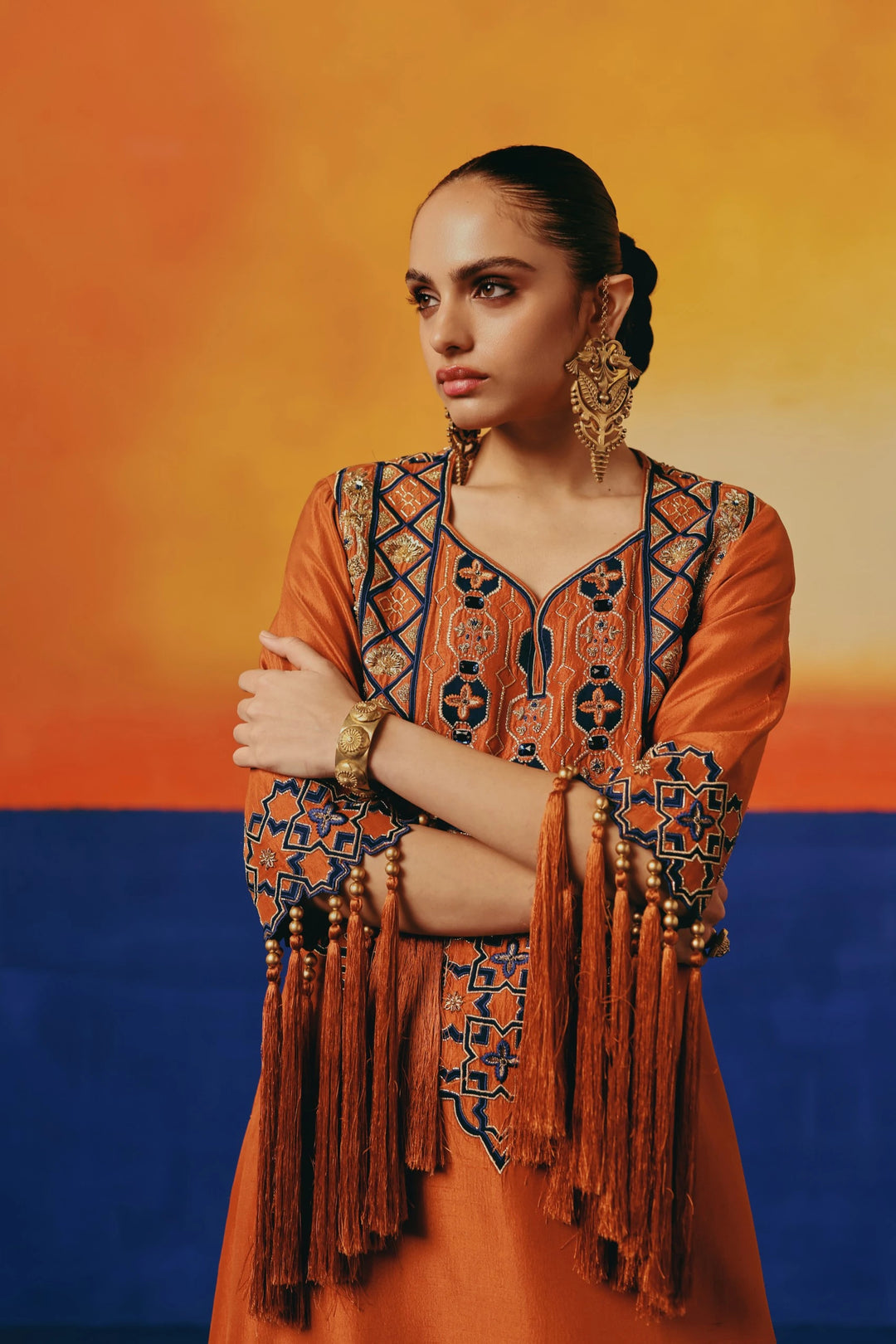 Close-up portrait of a model in Warra's orange silk kaftan with gold lattice embroidery, statement gold earrings