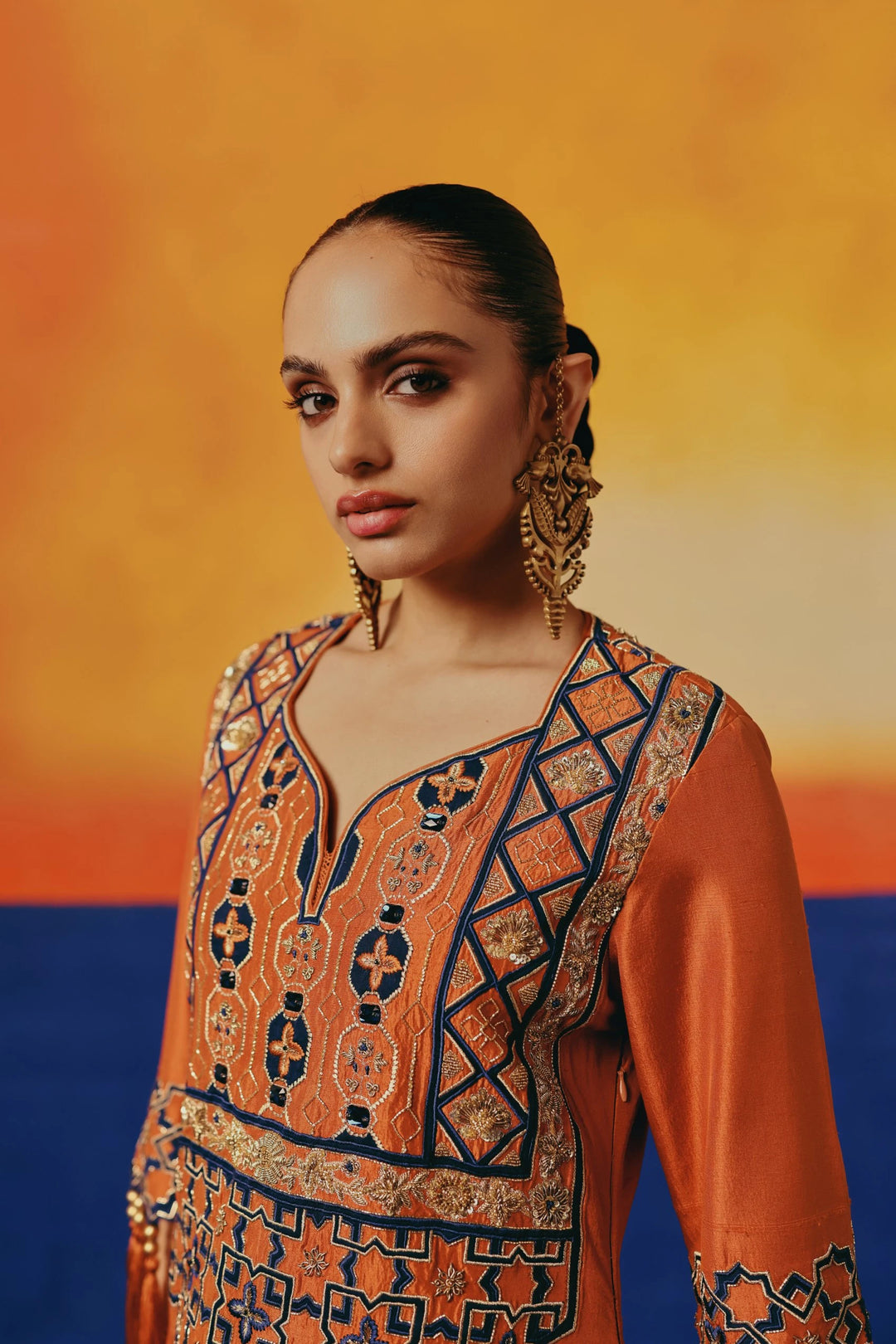 Close-up of the bodice of Warra's orange silk kaftan showing navy-and-gold geometric embroidery along the neckline
