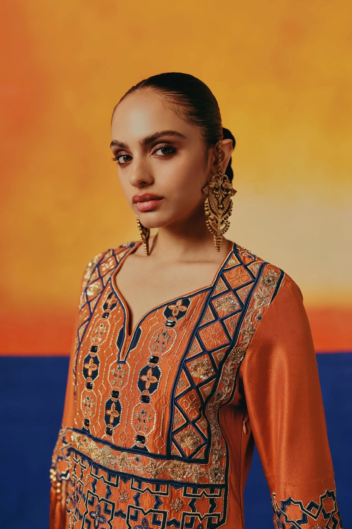 Close-up of the bodice of Warra's orange silk kaftan showing navy-and-gold geometric embroidery along the neckline