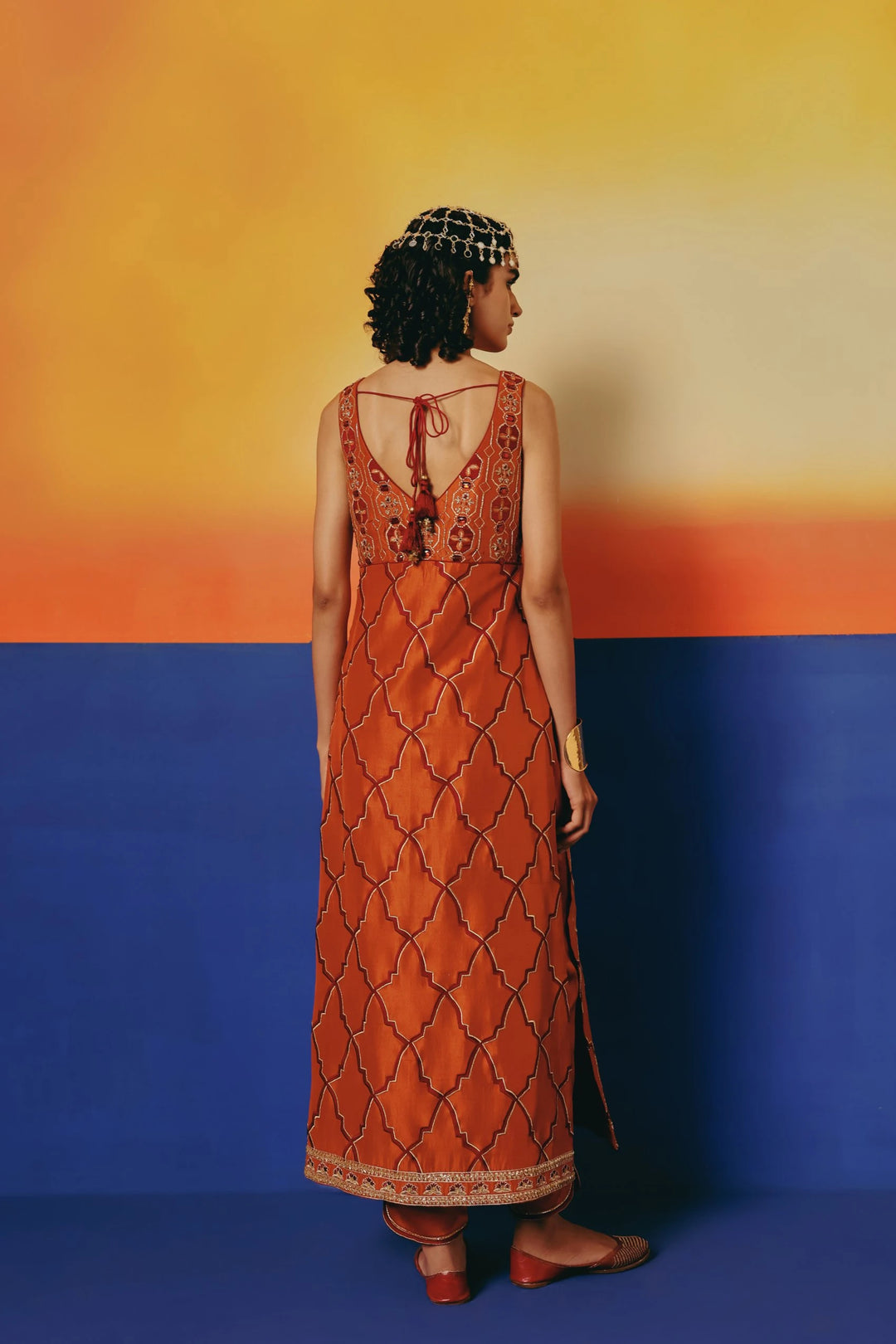 Back view of a model in Warra's rust-orange silk kurta showing gold lattice embroidery and a low tie-back neckline