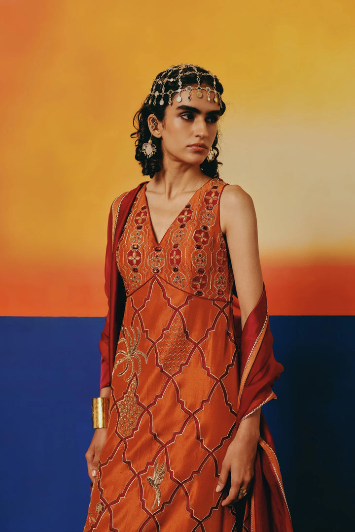 Three-quarter view of a model in Warra's rust-orange silk kurta showing gold lattice embroidery with palm tree and bird motifs