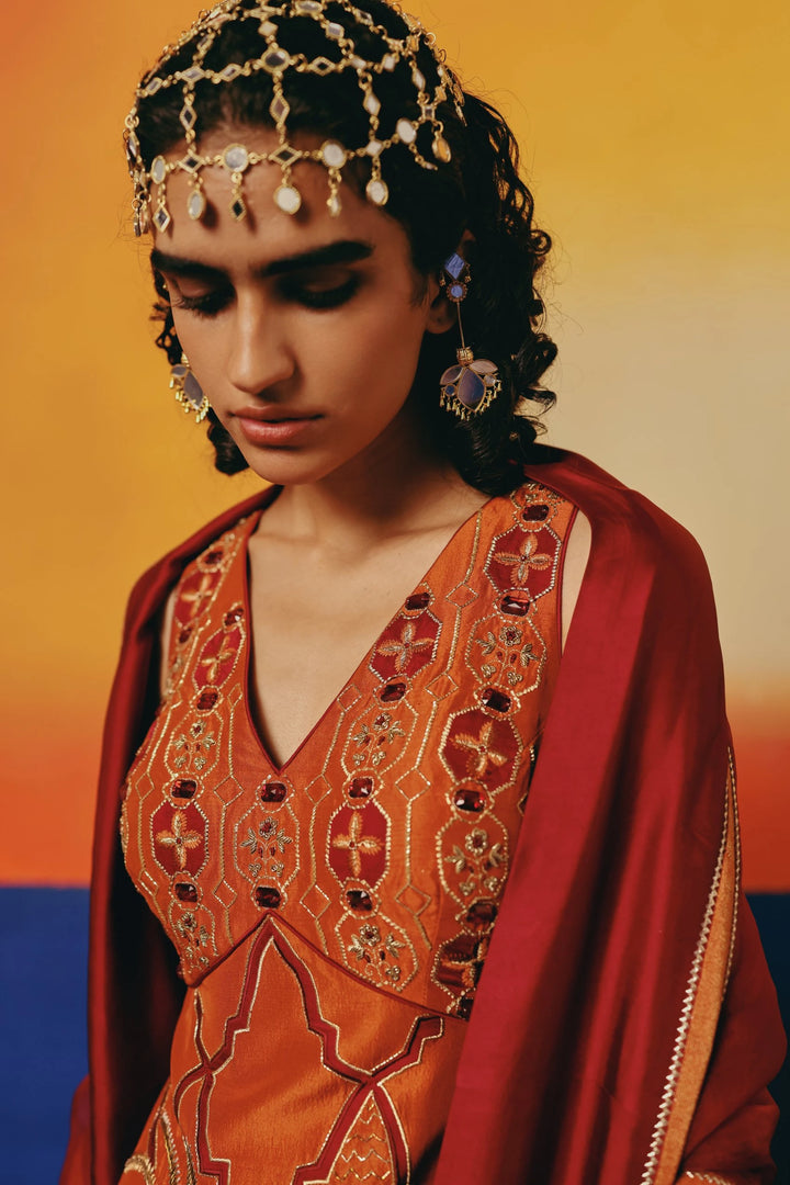 Close-up of a model wearing a gold mirror-work headpiece and Warra's rust-orange embroidered kurta with a red dupatta