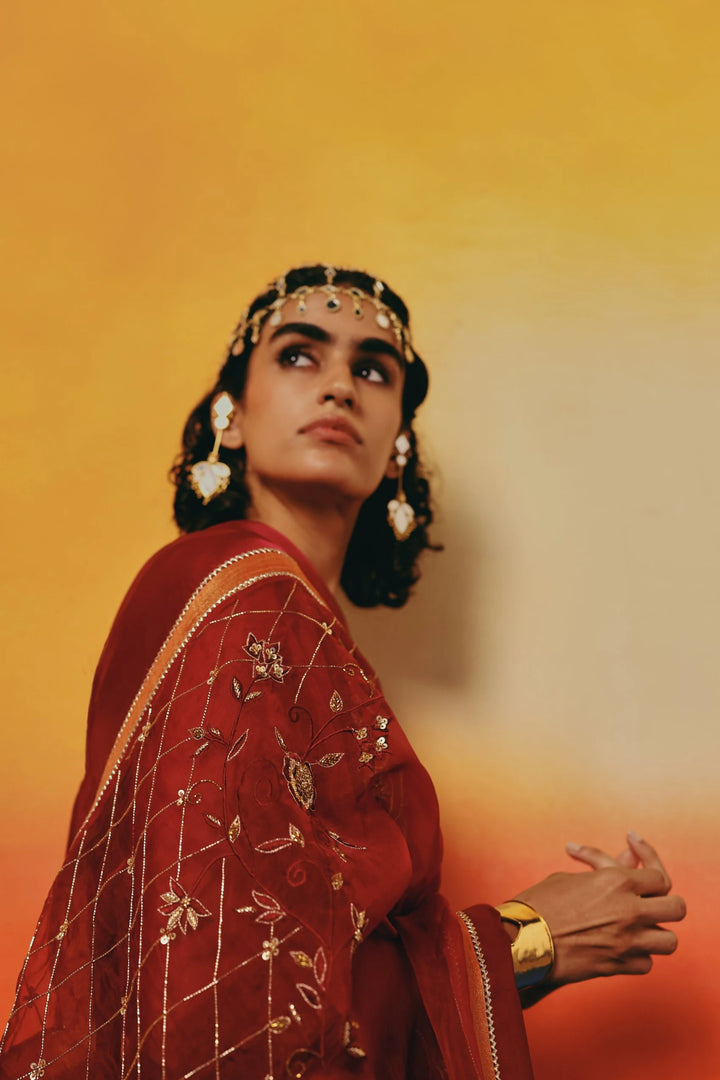 Close-up profile portrait of a model in Warra's rust-orange kurta, wearing a jewelled headpiece and a draped red dupatta