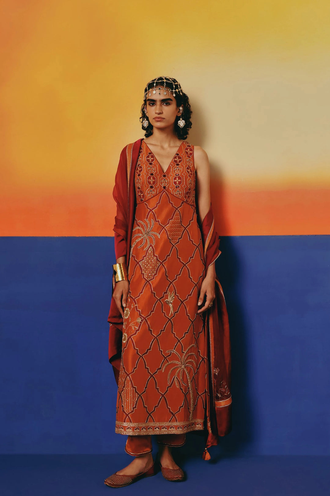 Full-length front view of a model in Warra's rust-orange silk kurta with gold lattice embroidery, palm tree and bird motifs, and a red dupatta