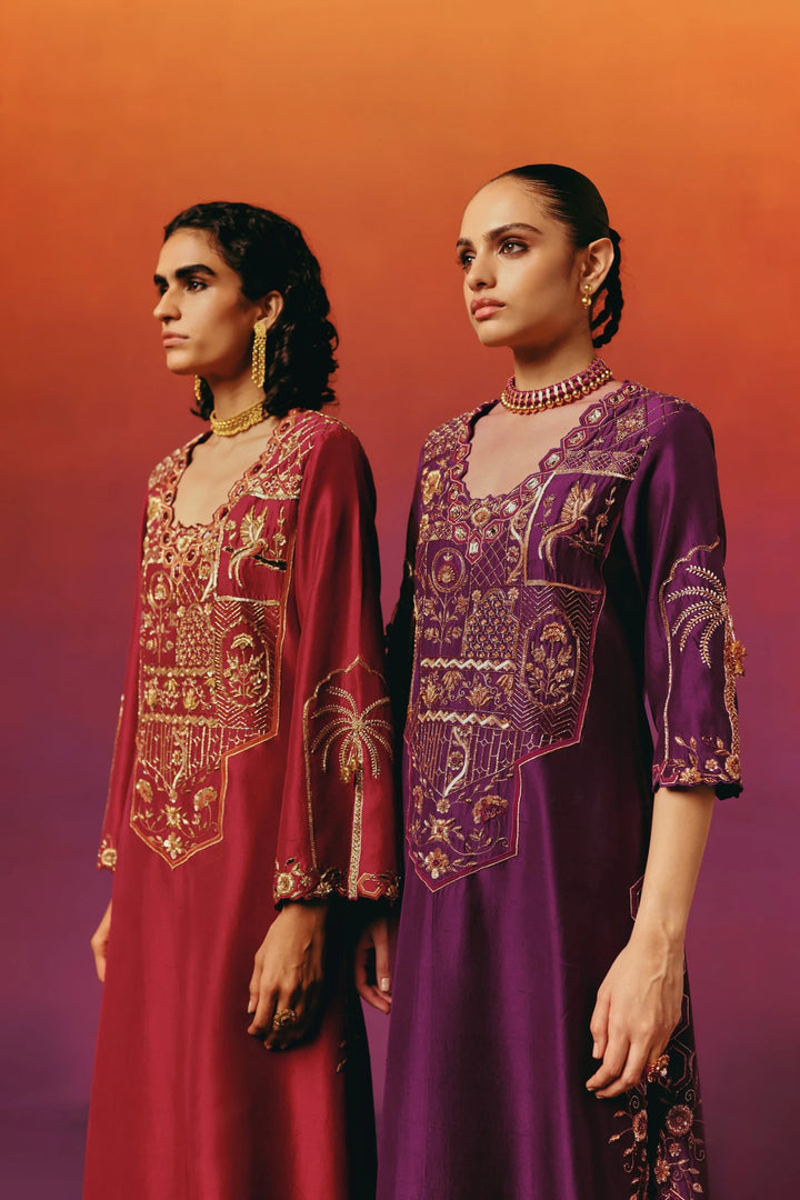 Two models in profile wearing Warra's red and purple silk kaftans, showing matching gold palm-tree embroidered sleeve cuffs and clasped hands