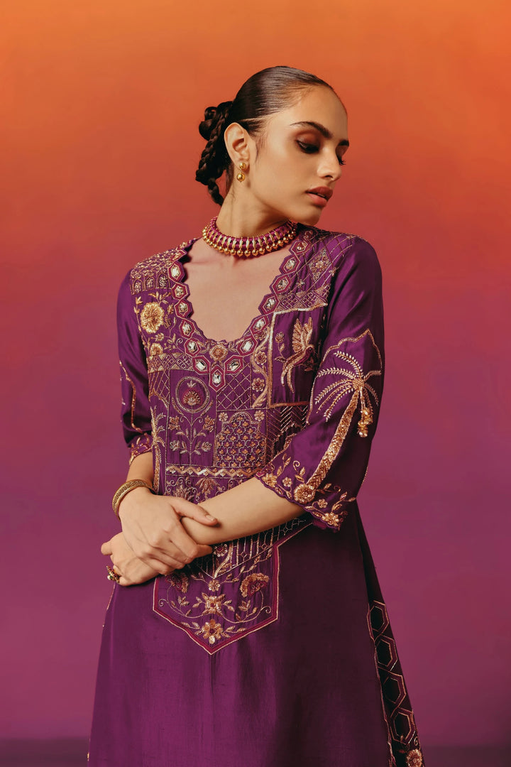 Close-up of a model in Warra's purple silk kaftan showing an intricately mirror-and-gold embroidered yoke with bird, palm-tree and floral motifs, paired with a beaded choker and layered gold bangles