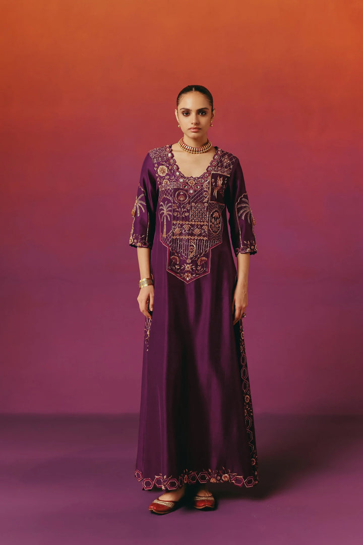Full-length front view of a model in Warra's deep purple silk kaftan with gold palm tree and bird embroidery on the bodice and hem