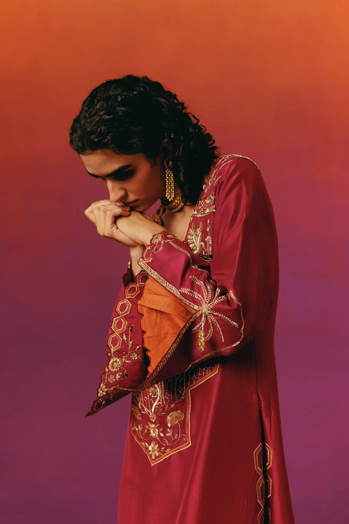 Close-up front view of a model in Warra's red silk kaftan showing a dense gold-and-mirror embroidered yoke with palm-tree, bird and floral motifs, paired with a gold choker