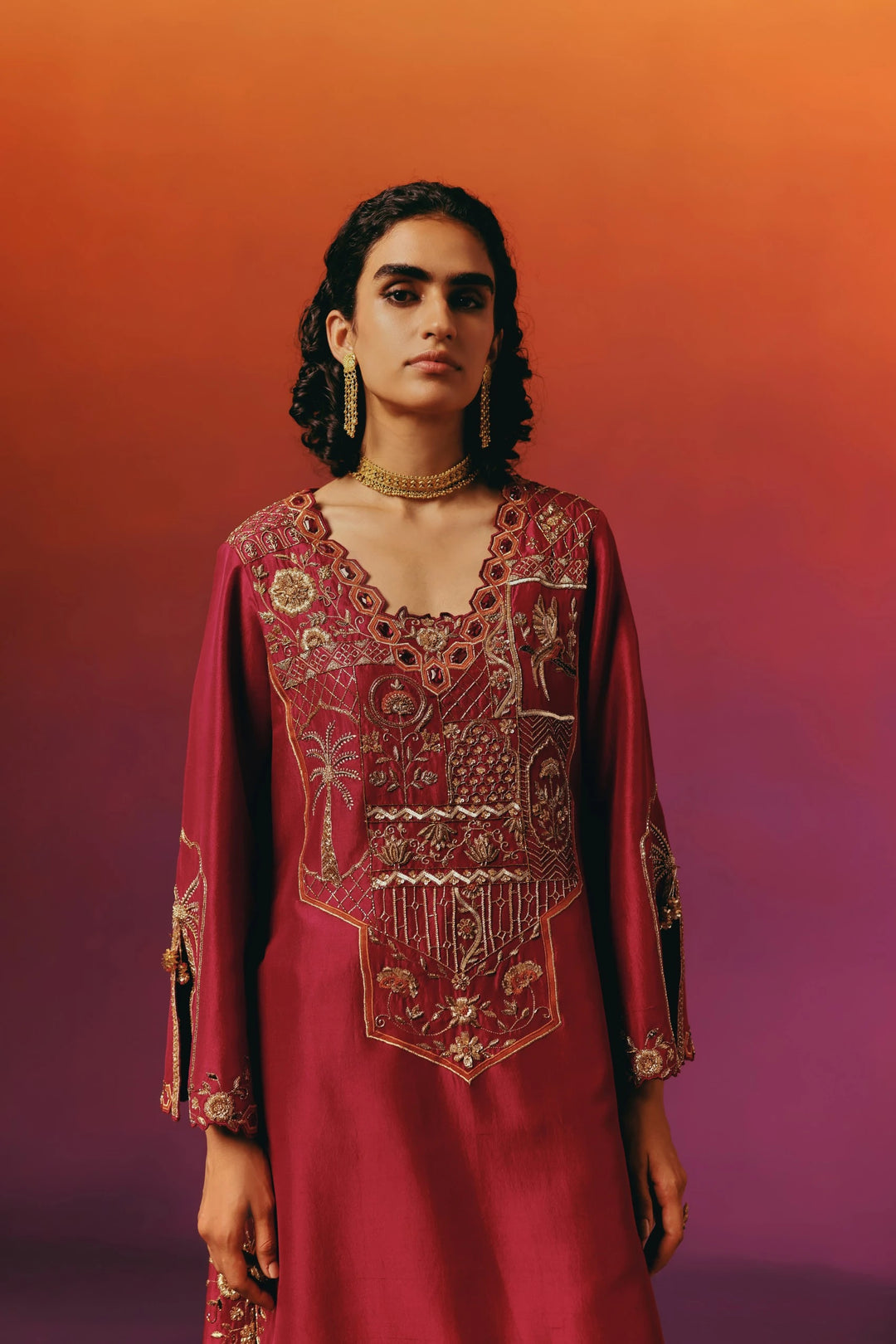 Close-up portrait of a model in Warra's red silk kaftan showing the gold embroidered yoke, tasselled gold drop earrings and a layered choker necklace
