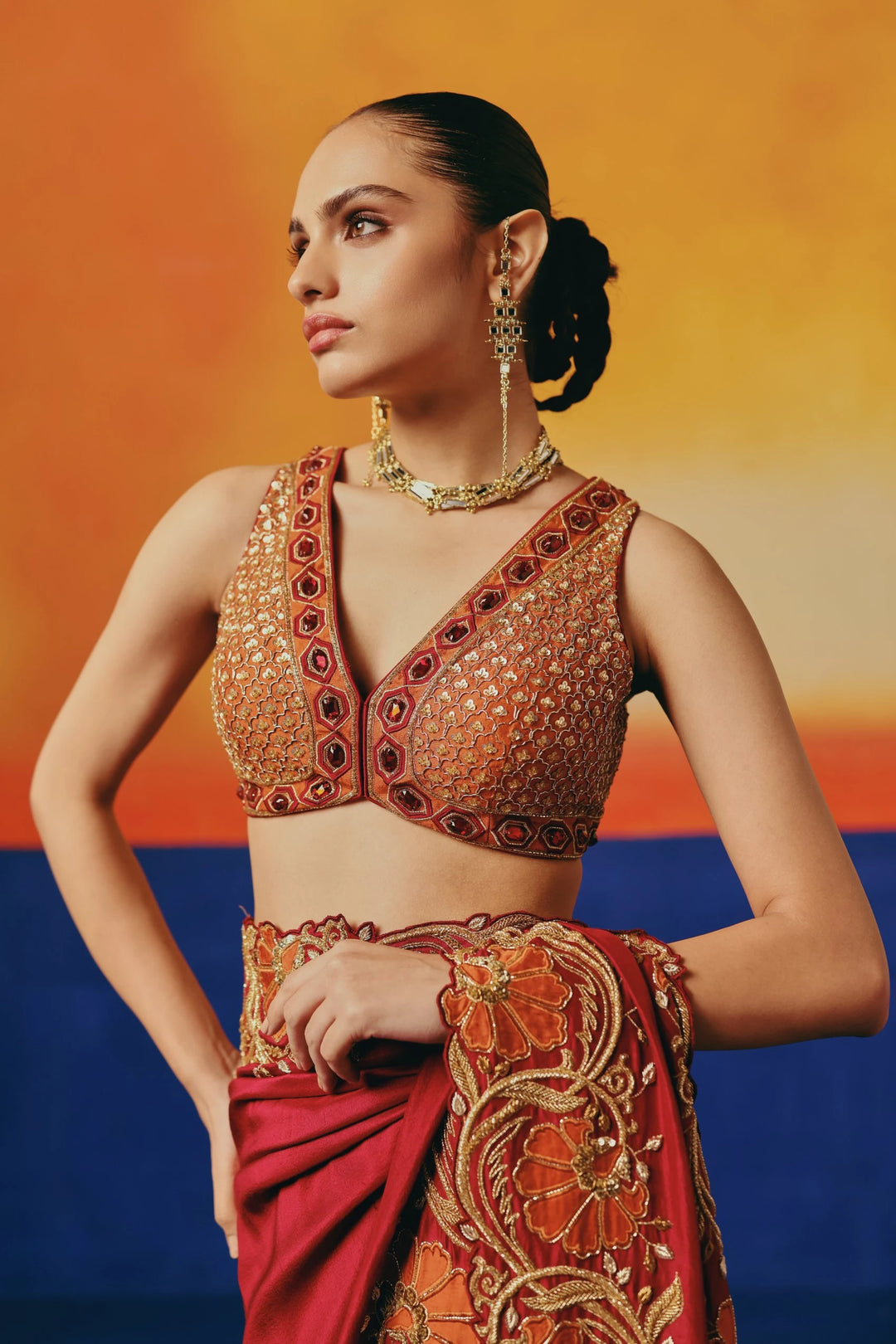 Close-up of Warra's mirror and stone-embellished one-shoulder blouse worn with a red silk saree featuring orange floral embroidery