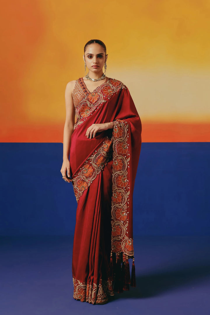 Full-length front view of a model in Warra's deep red silk saree with orange floral embroidery and a one-shoulder mirror-work blouse