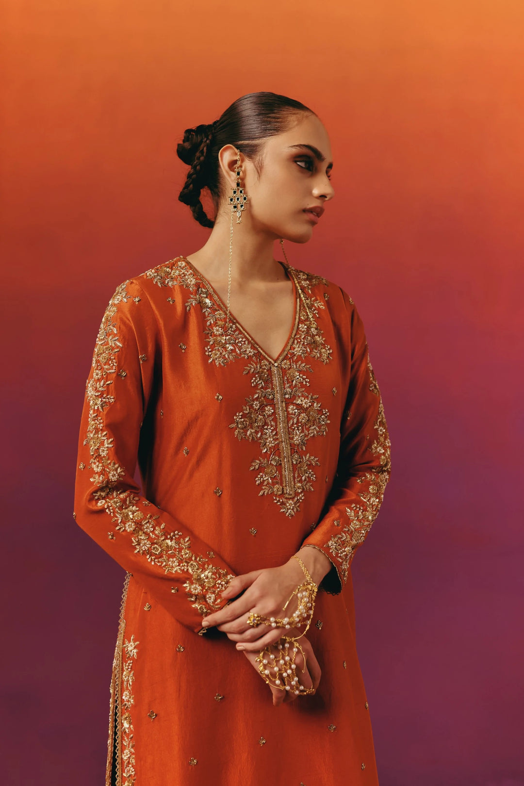 Close-up of the V-neckline of Warra's rust-orange silk kurta with dense gold floral embroidery, a statement drop earring and pearl bracelet