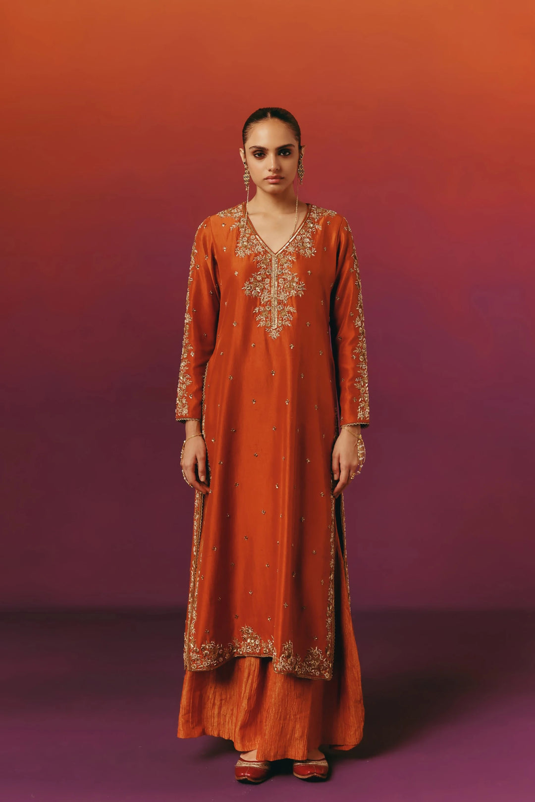 Front view of a model in Warra's rust-orange silk kurta with gold floral embroidery, worn with a matching dupatta and sharara