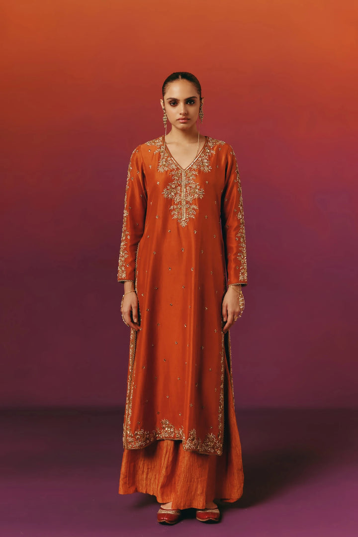 Front view of a model in Warra's rust-orange silk kurta with gold floral embroidery, worn with a matching dupatta and sharara